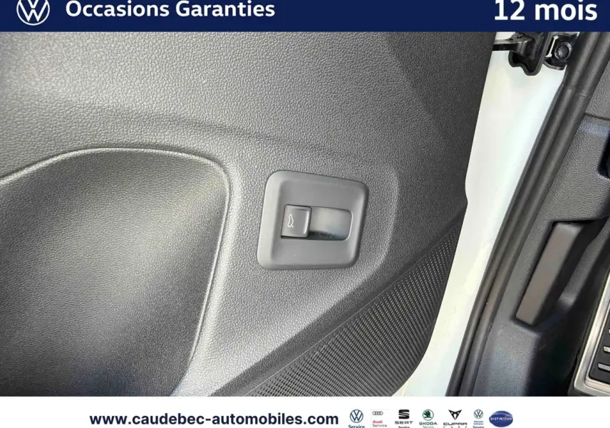 Gros plan sur le bouton d'ouverture du hayon dans l'encadrement de porte côté conducteur d'un Volkswagen T-Roc blanc.