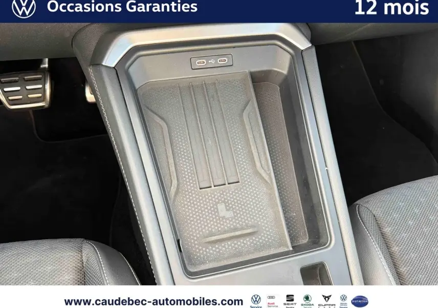Vue rapprochée de la console centrale noire du Volkswagen T-Roc 2025 avec zone de recharge sans fil et ports USB.
