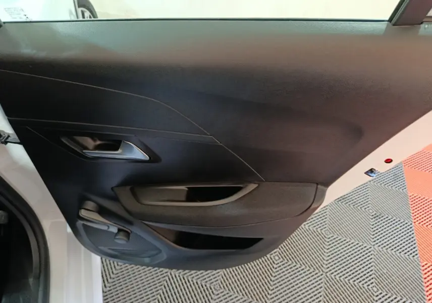 Vue intérieure de la porte arrière gauche noire d'une Peugeot 208 électrique blanche, avec poignée et commande de vitre manuelle.
