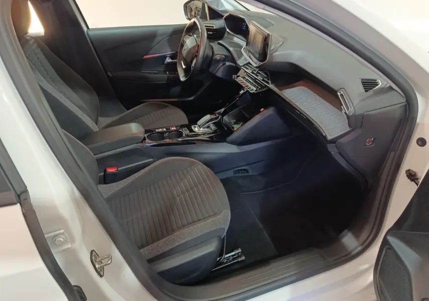 Vue intérieure côté conducteur de la Peugeot 208 électrique blanche, avec volant cuir multifonctions et tableau de bord digital.