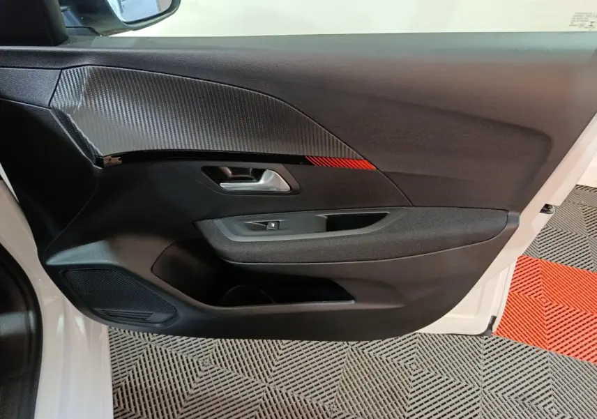 Vue intérieure côté gauche de la porte avant d'une Peugeot 208 électrique blanche avec insert décoratif noir et rouge.