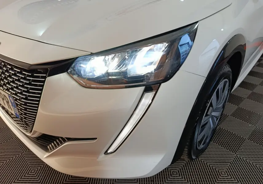 Gros plan sur l'avant droit blanc d'une Peugeot 208 électrique Active Business avec phares LED allumés.