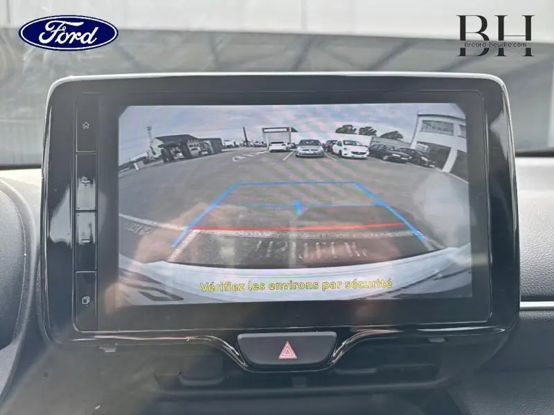 Écran tactile intérieur montrant la caméra de recul avec vue arrière du parking, tableau de bord noir brillant.