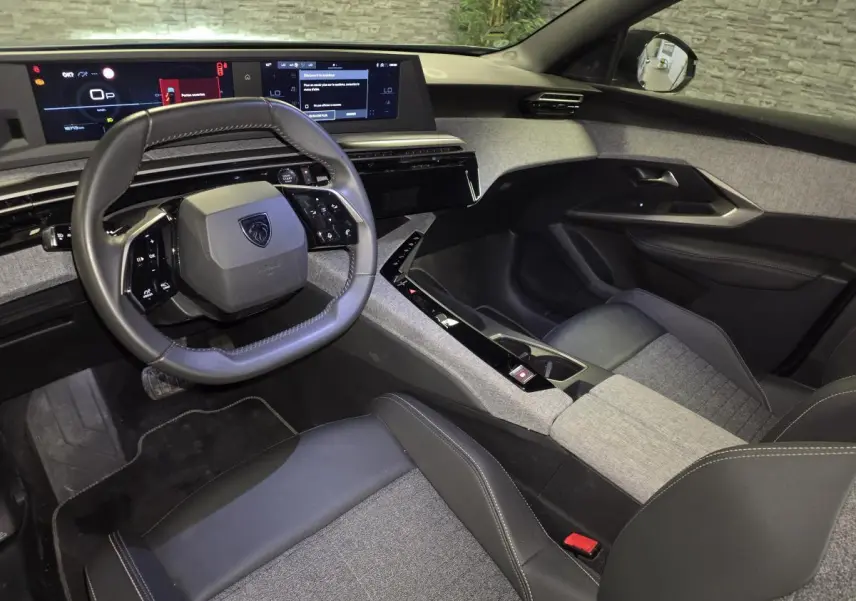 Intérieur avant droit du Peugeot 5008 2025 avec volant compact, sellerie tissu gris et cuir noir, et double écran HD panoramique.
