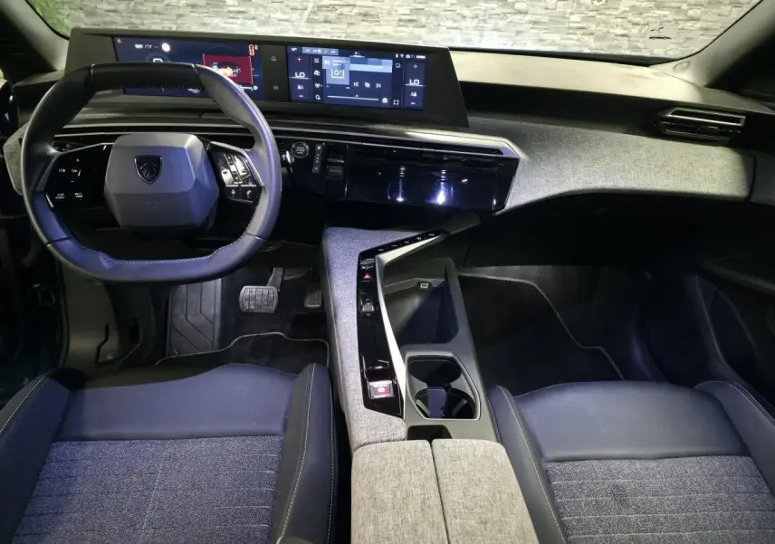 Vue intérieure avant du Peugeot 5008 2025, avec tableau de bord numérique, volant compact et sellerie tissu gris et noir.