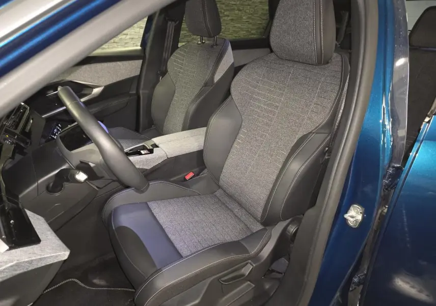 Vue intérieure côté conducteur du Peugeot 5008 bleu 2025, sièges tissu gris et cuir noir avec surpiqûres contrastées.