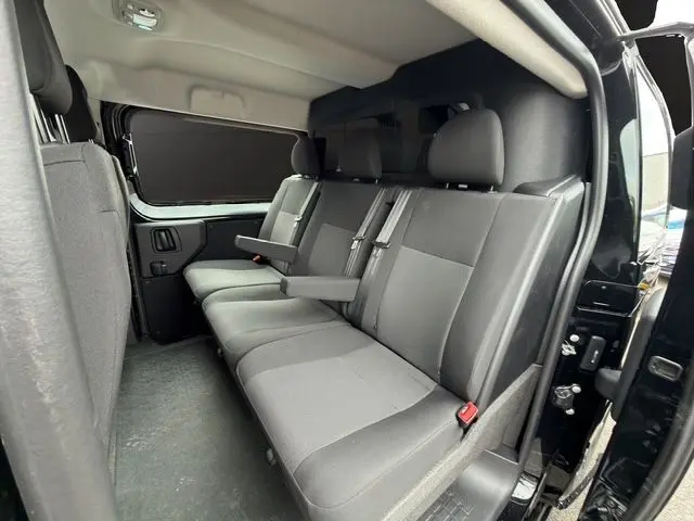 Vue intérieure côté droit du Citroën Jumpy noir 2025 montrant la banquette arrière 3 places avec accoudoirs et cloison vitrée.