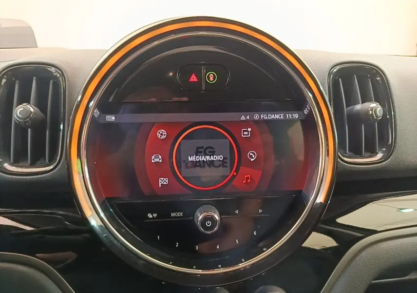 Vue rapprochée du tableau de bord de la MINI Countryman gris clair, avec écran tactile circulaire et éclairage orange.