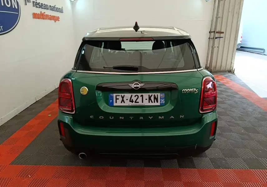 Vue arrière d'une MINI Countryman Cooper S vert foncé avec toit blanc, dans un garage éclairé.