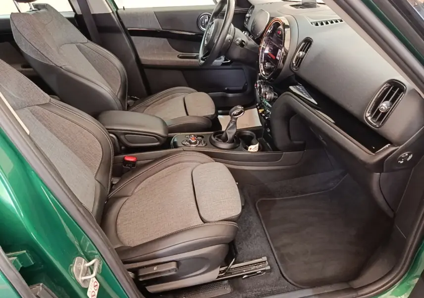 Vue intérieure côté conducteur d'une MINI Countryman Cooper SE avec sièges tissu gris et détails noirs, tableau de bord moderne.