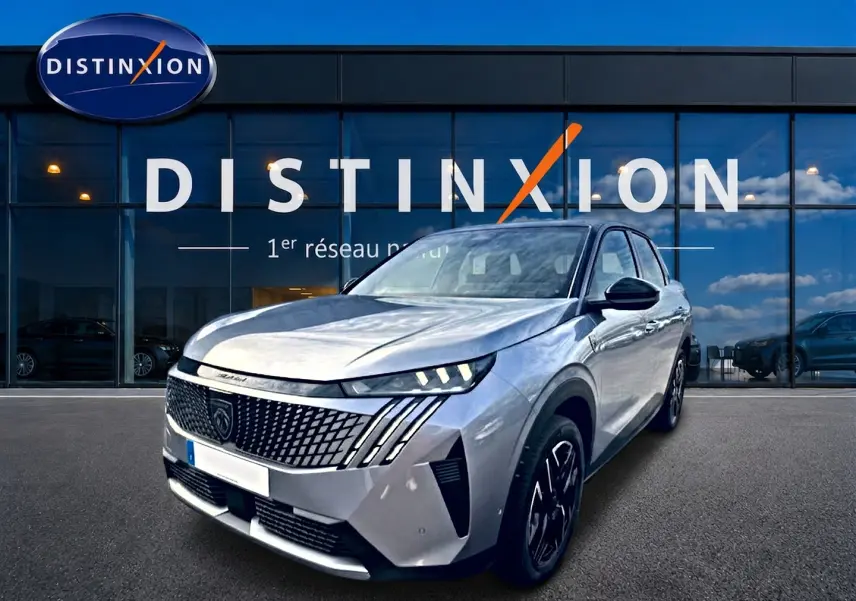 Peugeot 3008 gris artense en 3/4 avant droit, avec calandre distinctive et phares LED allumés, devant un showroom Distinxion.