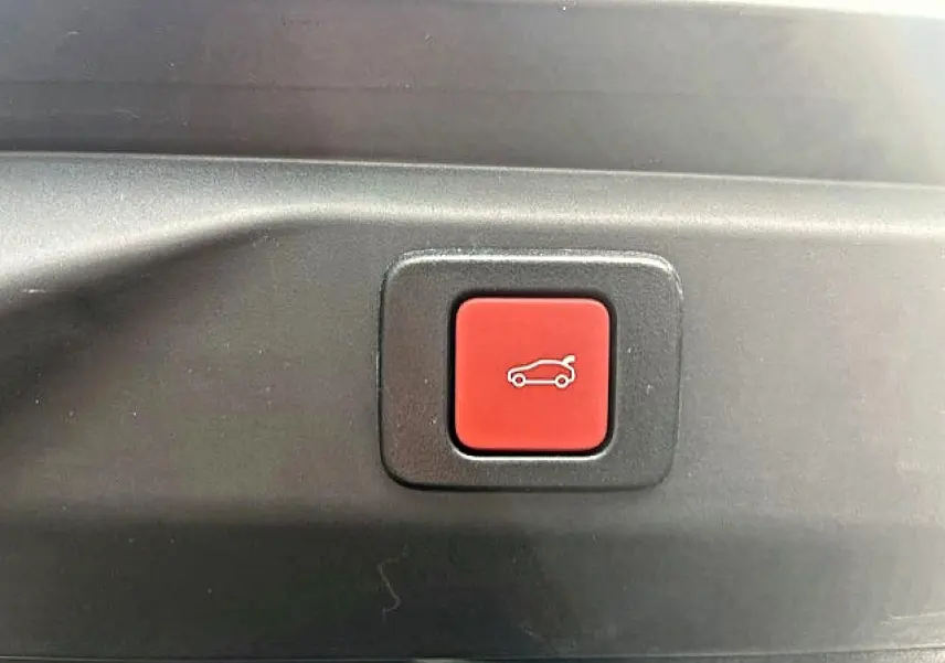 Gros plan sur le bouton rouge d'ouverture électrique du coffre du Peugeot 3008 gris Artense, intérieur coffre visible.