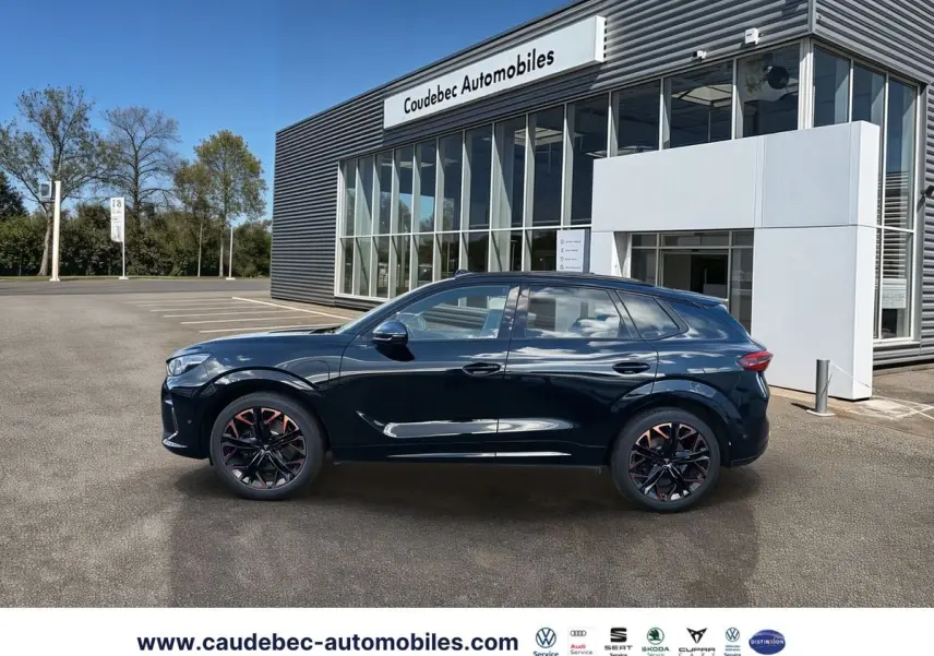 Vue de profil côté gauche d'une CUPRA Terramar noire avec jantes alliage 20 pouces cuivrées, stationnée devant un showroom.