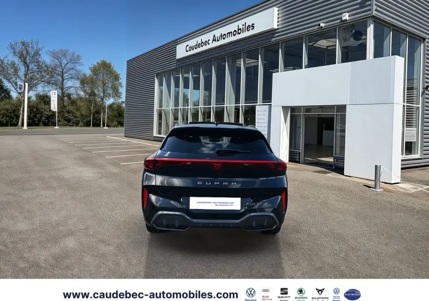 Vue arrière d'une CUPRA Terramar noire 2024, avec feux arrière continus et logo CUPRA lumineux, devant un bâtiment moderne.