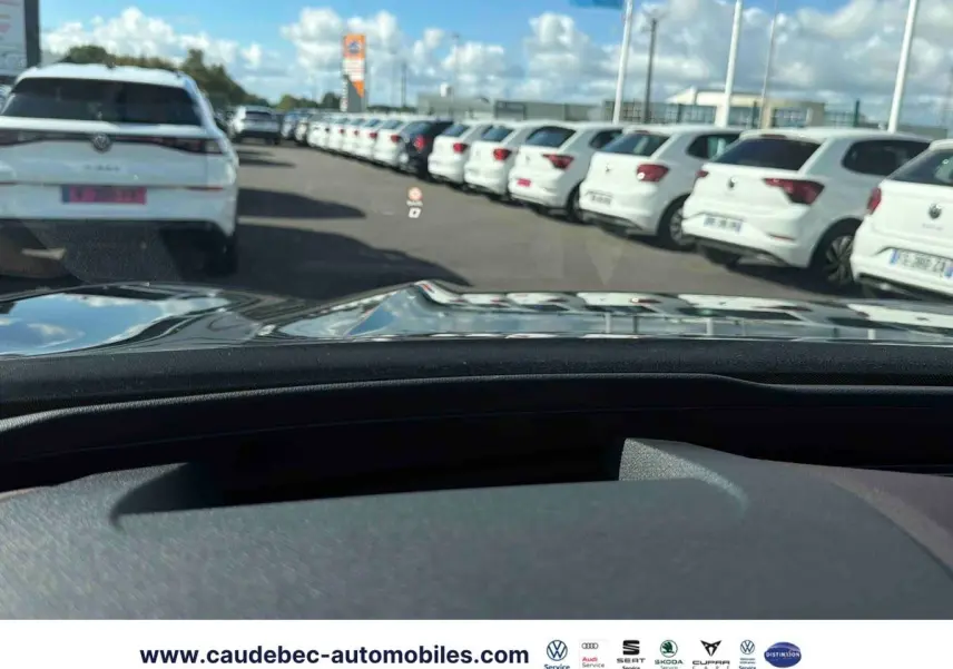 Vue depuis l’habitacle d’une CUPRA TERRAMAR noire, avec le capot et un parking de voitures blanches en arrière-plan.