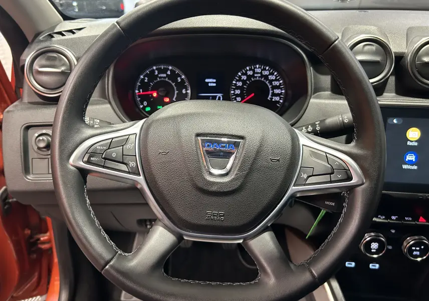 Vue centrée sur le volant du Dacia Duster 2022 orange Arizona, avec commandes intégrées et tableau de bord visible.