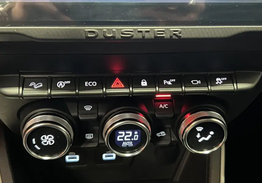 Gros plan sur la console centrale du Dacia Duster 2022 orange Arizona, montrant les commandes de climatisation et les boutons de fonction.