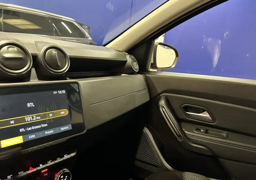 Intérieur côté passager du Dacia Duster 2022, tableau de bord et porte avec finitions noires et écran tactile allumé.