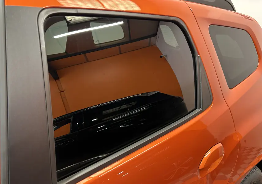 Vue latérale arrière droite du Dacia Duster 2022 orange Arizona avec vitres teintées et poignée de porte intégrée.
