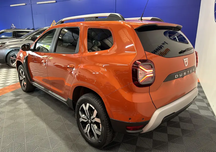 Vue 3/4 arrière droite du Dacia Duster orange Arizona 2022 avec feux arrière LED et barres de toit visibles.