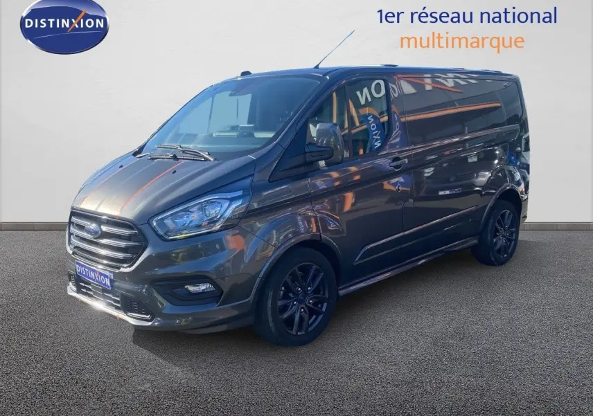 Ford Transit Custom Fourgon gris magnetic en 3/4 avant droit, avec jantes noires et calandre chromée visible.