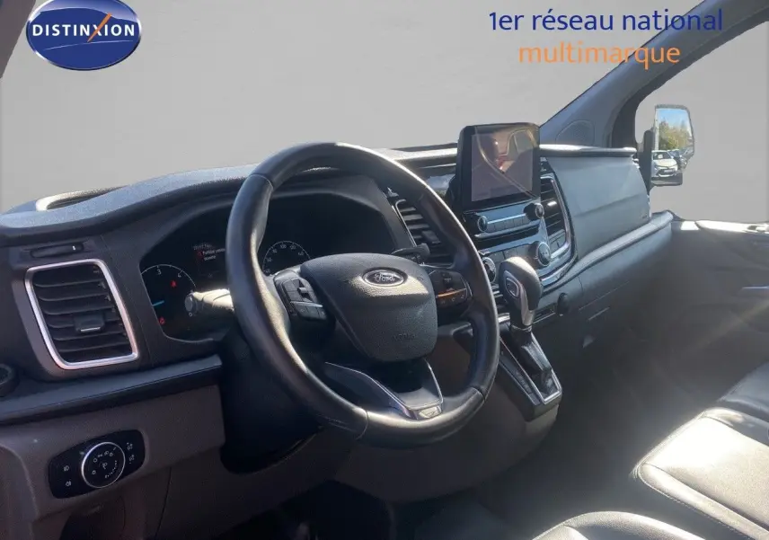 Vue intérieure du poste de conduite du Ford Transit Custom gris, avec volant cuir et écran tactile central.