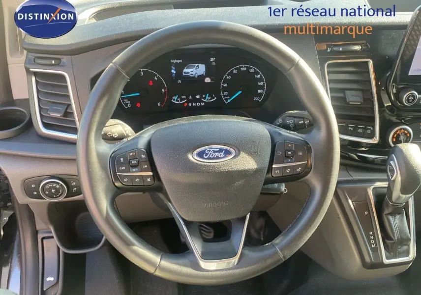 Vue rapprochée du volant et du tableau de bord du Ford Transit Custom gris Magnetic, avec levier de vitesses automatique visible.