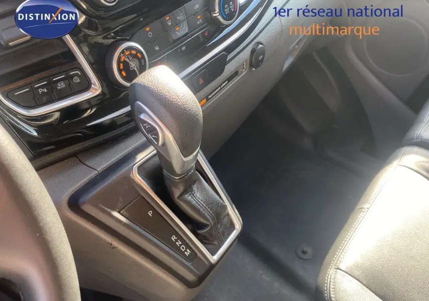 Gros plan sur la console centrale du Ford Transit Custom gris, mettant en valeur le levier de vitesse automatique et les commandes climatiques.