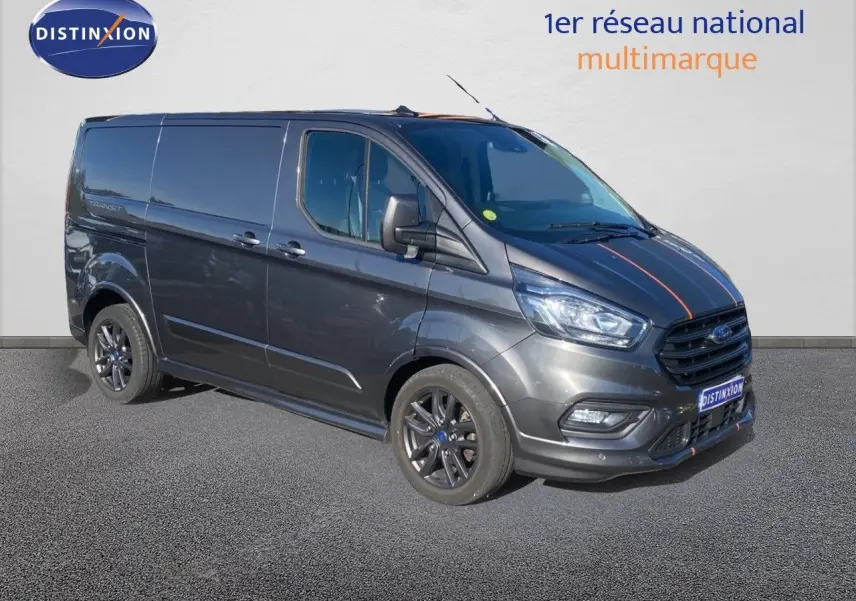 Fourgon Ford Transit Custom gris magnetic en 3/4 avant droit avec jantes noires et bandes décoratives rouges sur le capot.