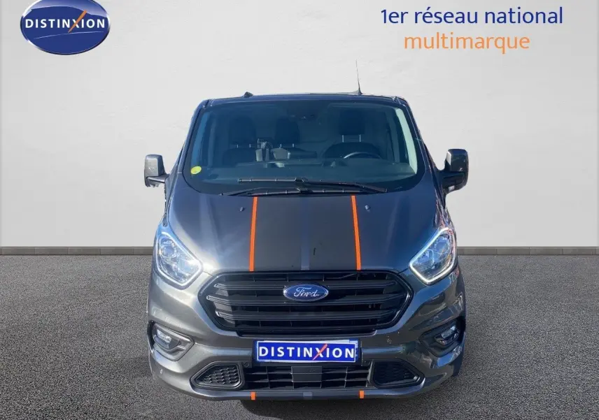 Vue frontale d'un Ford Transit Custom gris magnetic avec bandes noires et orange sur le capot, calandre noire.
