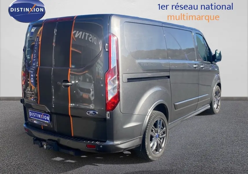 Vue 3/4 arrière droit du Ford Transit Custom gris magnetic avec jantes sport et bandes orange sur les portes arrière.