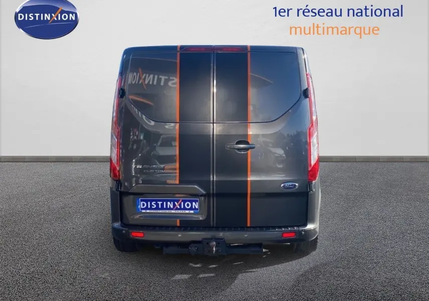 Vue arrière d'un Ford Transit Custom gris magnetic avec bandes orange verticales et attelage visible.