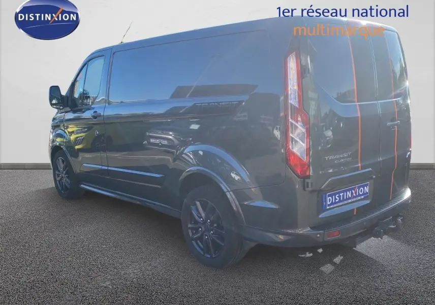 Vue 3/4 arrière droite du Ford Transit Custom gris magnetic avec bandes orange et jantes noires sport.