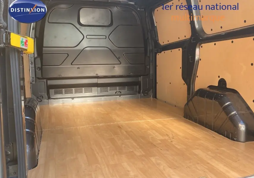 Vue intérieure du fourgon Ford Transit Custom L1H1 2023, montrant l'espace de chargement avec plancher bois clair et parois protégées.