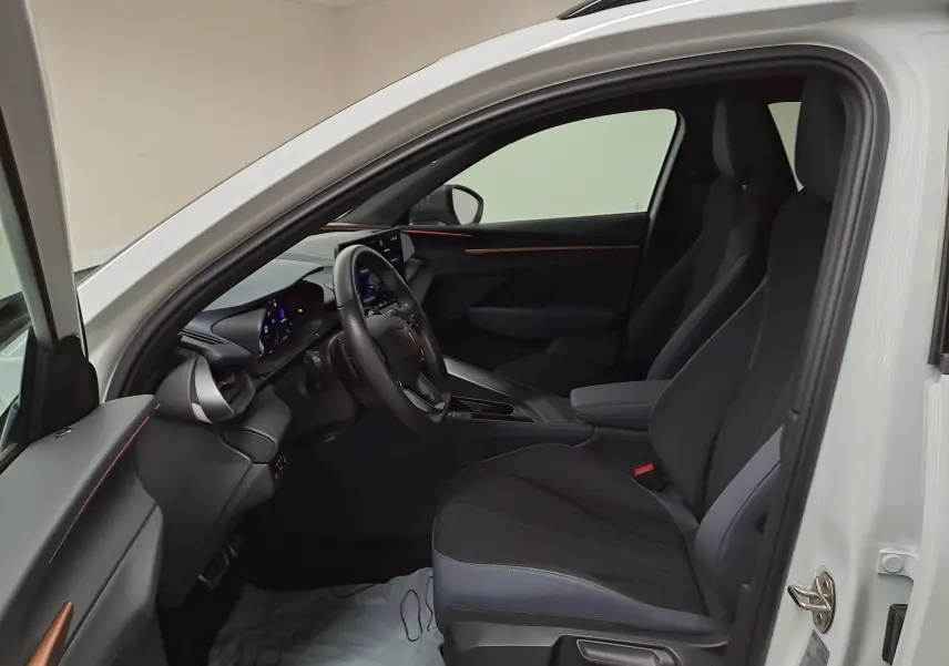 Vue intérieure côté conducteur de la CUPRA TERRAMAR blanc Nevada, avec sièges noirs et tableau de bord moderne.