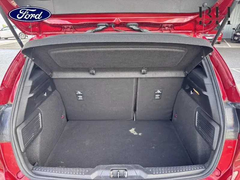 Coffre ouvert vu de l'arrière d'une Ford Focus 1.0 EcoBoost rouge, montrant un espace de chargement propre et spacieux.