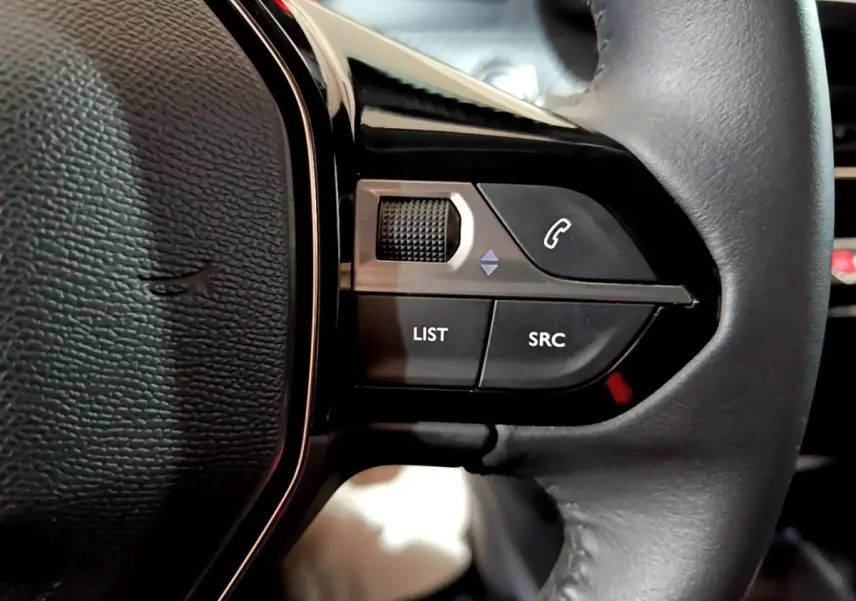 Gros plan sur les commandes gauche du volant cuir de la Peugeot 208 électrique blanche, boutons list, SRC et appel.