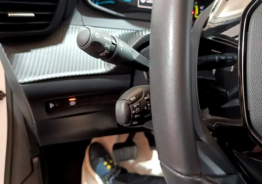 Gros plan sur le volant noir et les commandes de régulateur de vitesse de la Peugeot 208 électrique, tableau de bord partiellement visible.