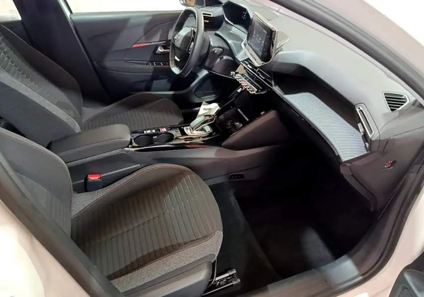 Intérieur avant droit de la Peugeot 208 électrique blanche, avec tableau de bord moderne et sièges gris à surpiqûres rouges.