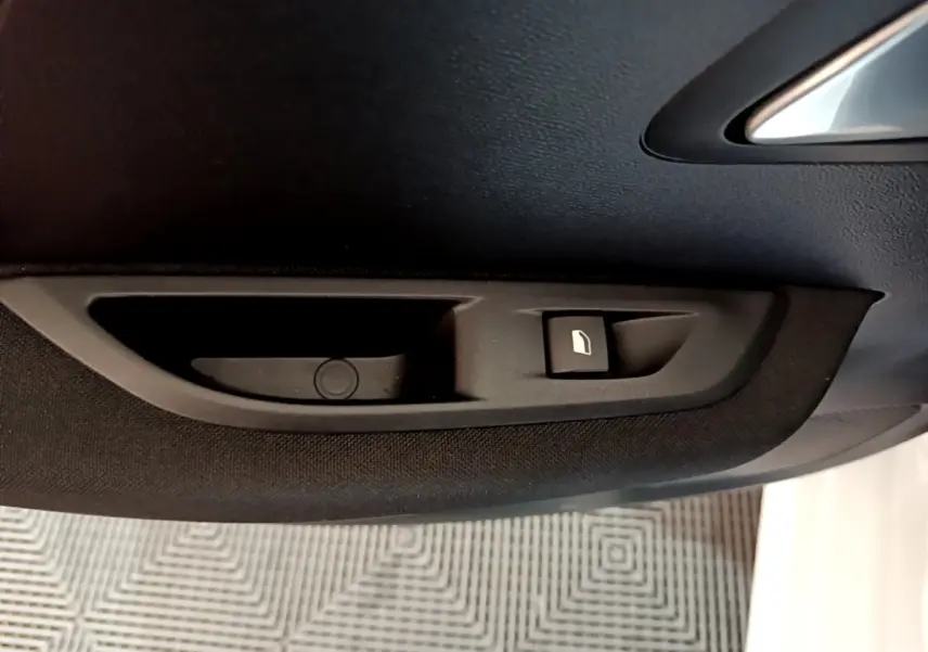 Détail intérieur du panneau de porte côté conducteur noir avec bouton de commande de vitre sur Peugeot 208 Electrique blanche.
