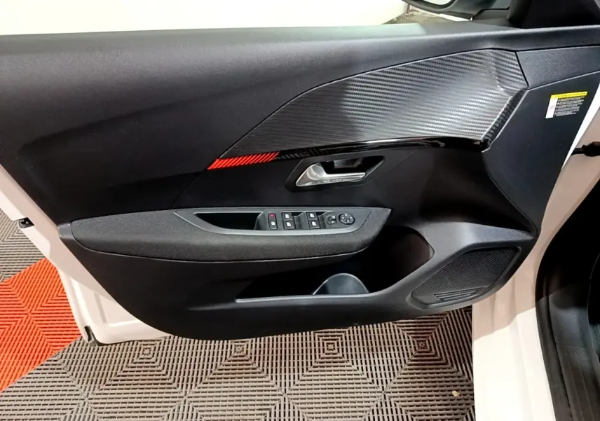 Vue intérieure côté gauche de la porte avant d’une Peugeot 208 électrique blanche avec insert carbone et bande rouge.