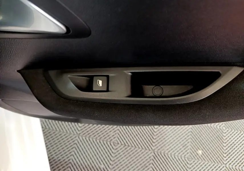 Bouton de commande de vitre électrique sur la porte intérieure noire d'une Peugeot 208 électrique blanche, vue côté conducteur.