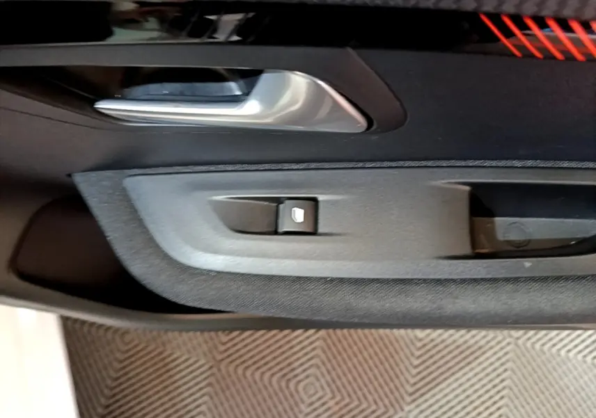 Gros plan sur la poignée intérieure et le bouton de lève-vitre côté conducteur de la Peugeot 208 électrique blanche.