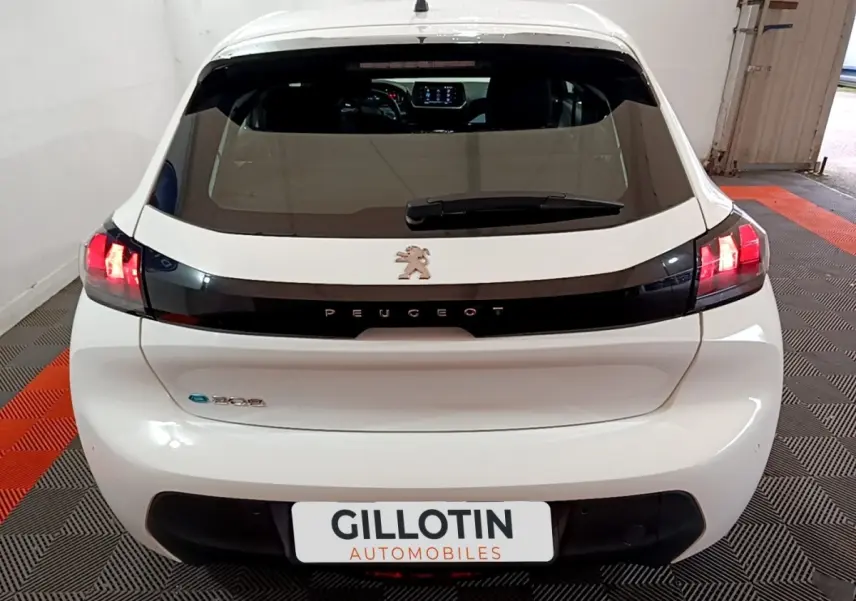 Vue arrière d'une Peugeot 208 électrique blanche avec feux LED allumés et bande noire distinctive sur le hayon.