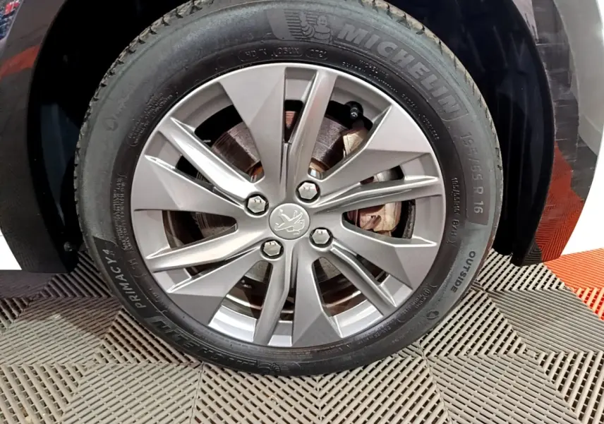 Gros plan sur la roue avant droite de la Peugeot 208 électrique blanche, jante alliage avec logo lion central.