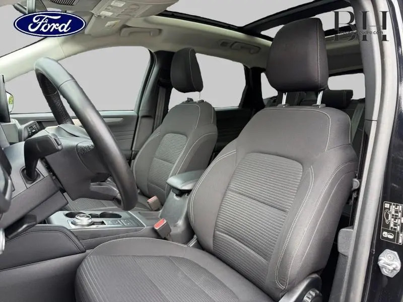 Vue intérieure côté conducteur du Ford Kuga 2023 noir Agate avec toit ouvrant panoramique et sièges sport en tissu noir.