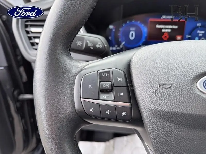 Gros plan sur le volant cuir multifonction côté gauche du Ford Kuga noir Agate 2023 avec commandes de régulateur et audio.