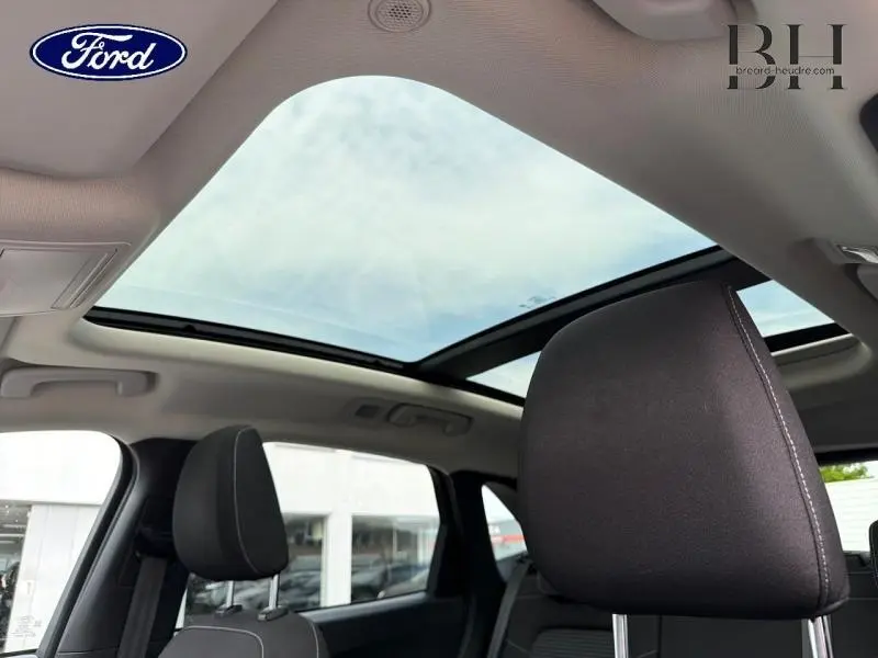 Vue intérieure du toit ouvrant panoramique électrique du Ford Kuga 2023, avec sièges noirs et ciel visible.