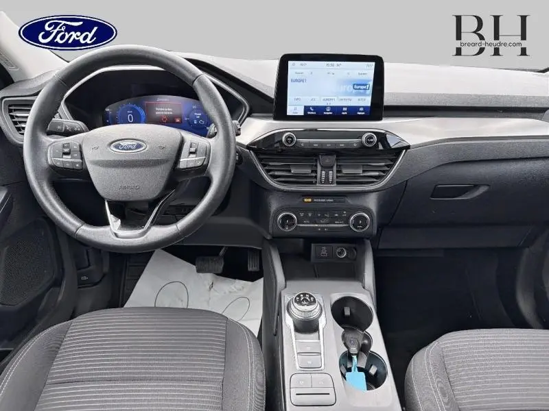 Vue intérieure avant du Ford Kuga 2023, tableau de bord et volant cuir multifonction avec écran tactile central.