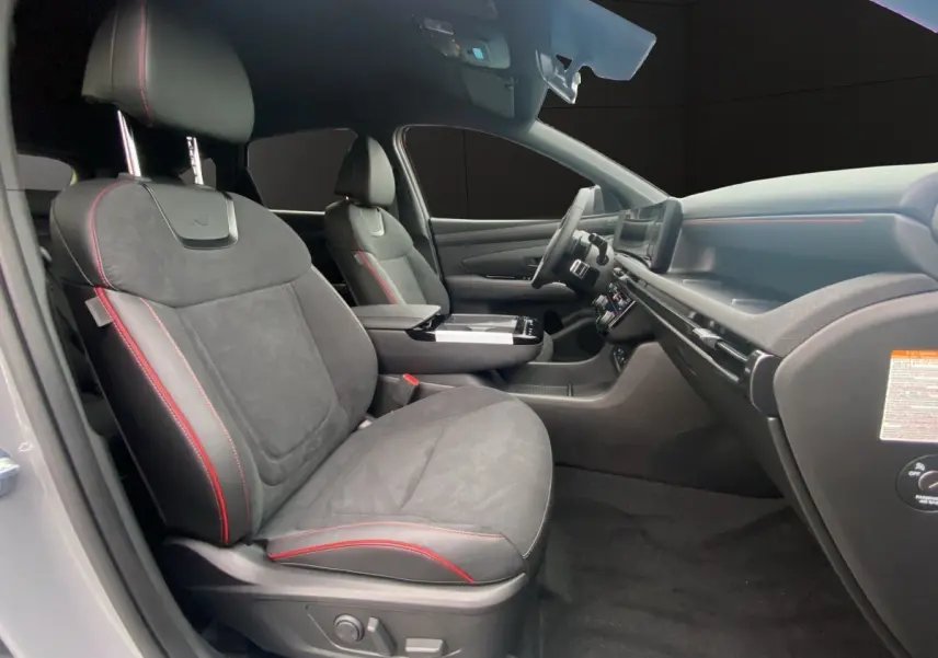 Intérieur avant du Hyundai Tucson gris foncé, sièges noirs avec surpiqûres rouges et tableau de bord moderne.